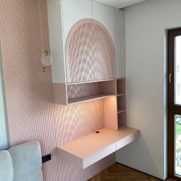 Deineka.pl - Różowo-białe biurko na wymiar z szafkami wiszącymi, oświetleniem i dekoracyjną ścianą z lameli. Widok na jasne wnętrze z parkietem.