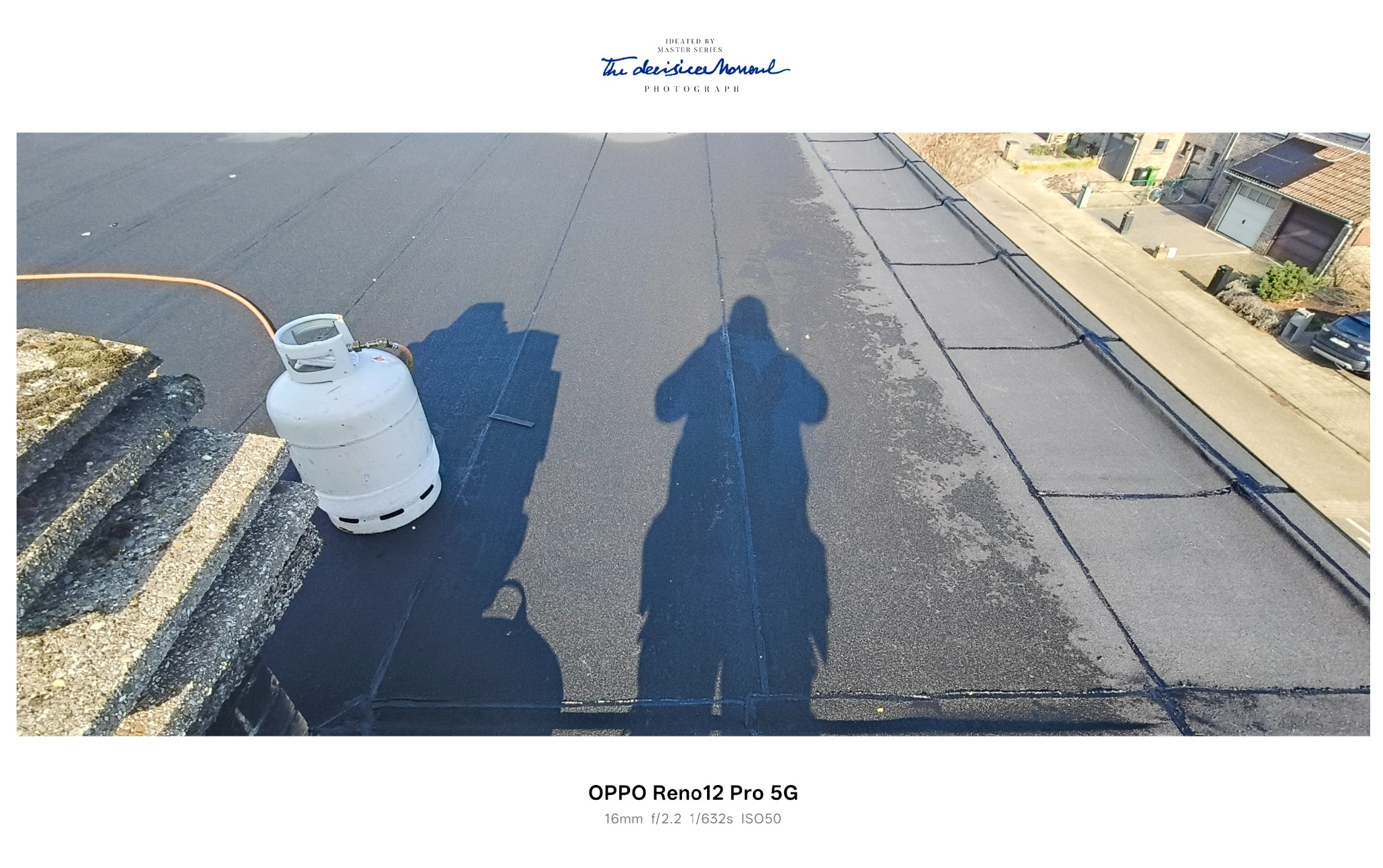 Czarny, płaski dach po renowacji z widocznym cieniem osoby i butlą gazową. W tle budynki mieszkalne. Widok z góry, ostre światło słoneczne.