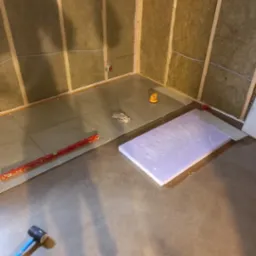 Przygotowanie do wykończenia łazienki: izolacja ścian wełną mineralną, ułożone płyty podłogowe, narzędzia pracy. Etap prac wykończeniowych z bliska.