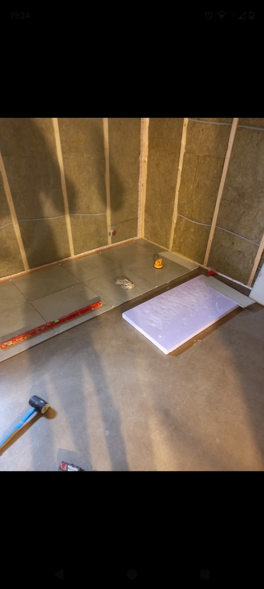 Przygotowanie do wykończenia łazienki: izolacja ścian wełną mineralną, ułożone płyty podłogowe, narzędzia pracy. Etap prac wykończeniowych z bliska.