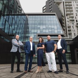 LIBERTY SPÓŁKA Z OGRANICZONĄ ODPOWIEDZIALNOŚCIĄ - Zespół doradców na tle nowoczesnej architektury biurowej, w eleganckich strojach, pozujący do zdjęcia grupowego. Ujęcie z dołu podkreśla dynamikę i profesjonalizm.