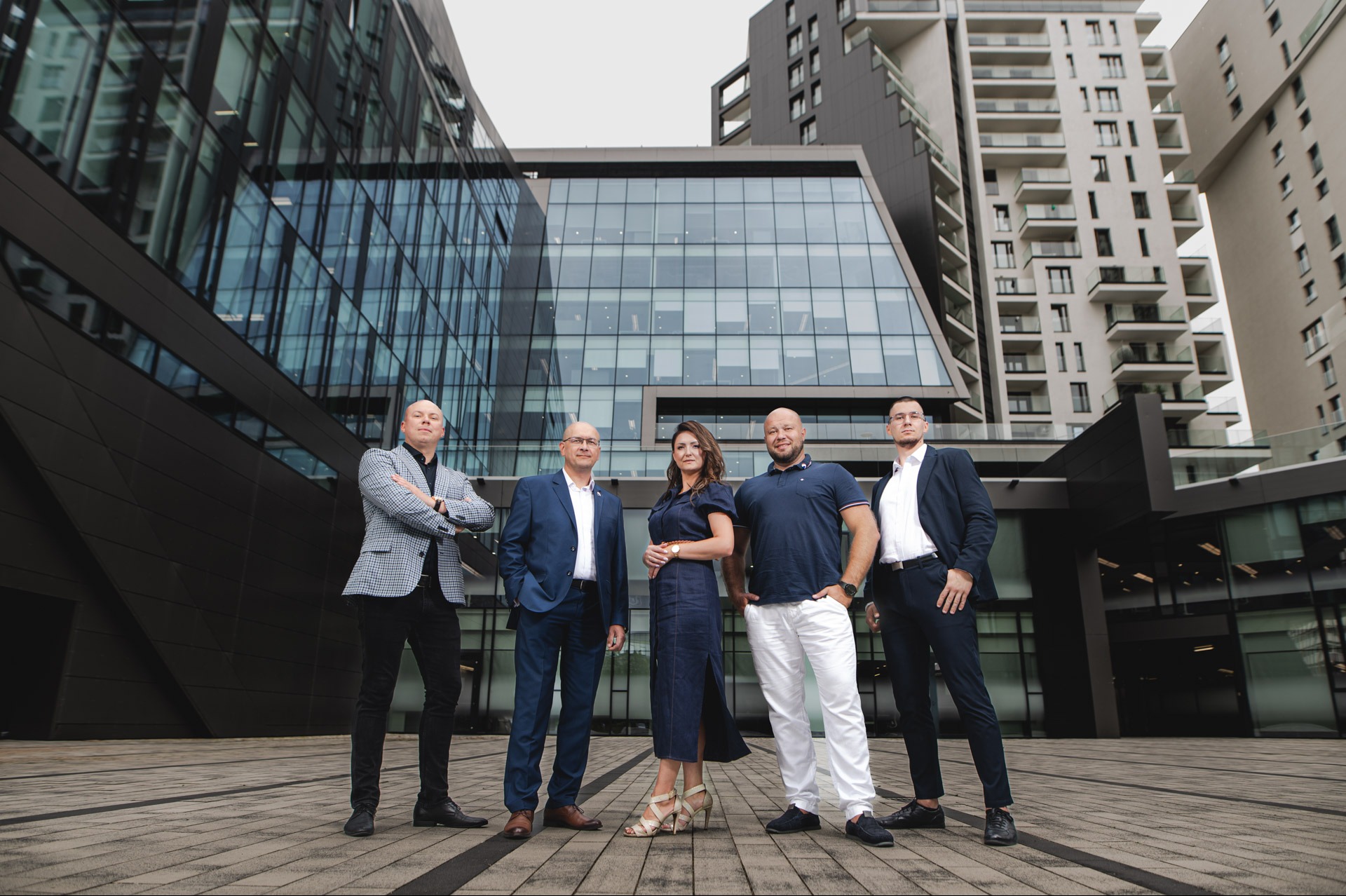 Zespół doradców na tle nowoczesnej architektury biurowej, w eleganckich strojach, pozujący do zdjęcia grupowego. Ujęcie z dołu podkreśla dynamikę i profesjonalizm.
