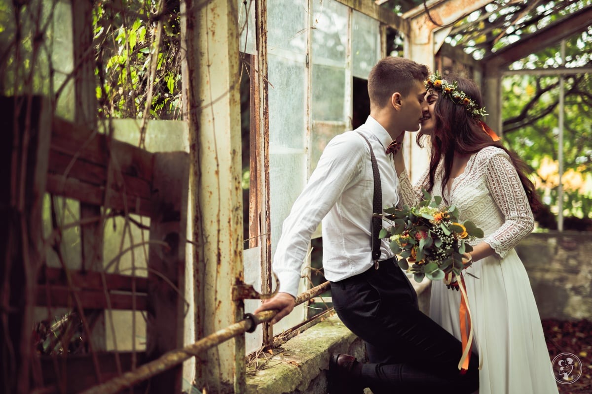 Pocałunek pary młodej w rustykalnej scenerii szklarni w Jeleniej Górze. Panna młoda z wiankiem i bukietem, pan młody w szelkach. Romantyczna sesja ślubna.