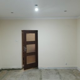 Le-Ma Bud Tomasz Gibas - Pokój po malowaniu ścian na kremowo, widoczne listwy przypodłogowe i sufitowe, otwarte drzwi z szybami. Podłoga surowa, przygotowana do dalszych prac wykończeniowych.