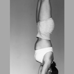 Hornest.gym - Czarno-białe zdjęcie kobiety w pozycji stania na rękach w minimalistycznym wnętrzu. Widoczne detale: biały top, szorty, skarpety i bransoletka. Upięte włosy.