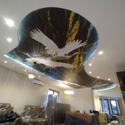 KS Perfect profesjonalne wykończenia wnętrz - Sufit w salonie z dekoracyjną, marmurkową aplikacją z motywem żurawi w locie. Meble zabezpieczone folią ochronną podczas prac wykończeniowych.