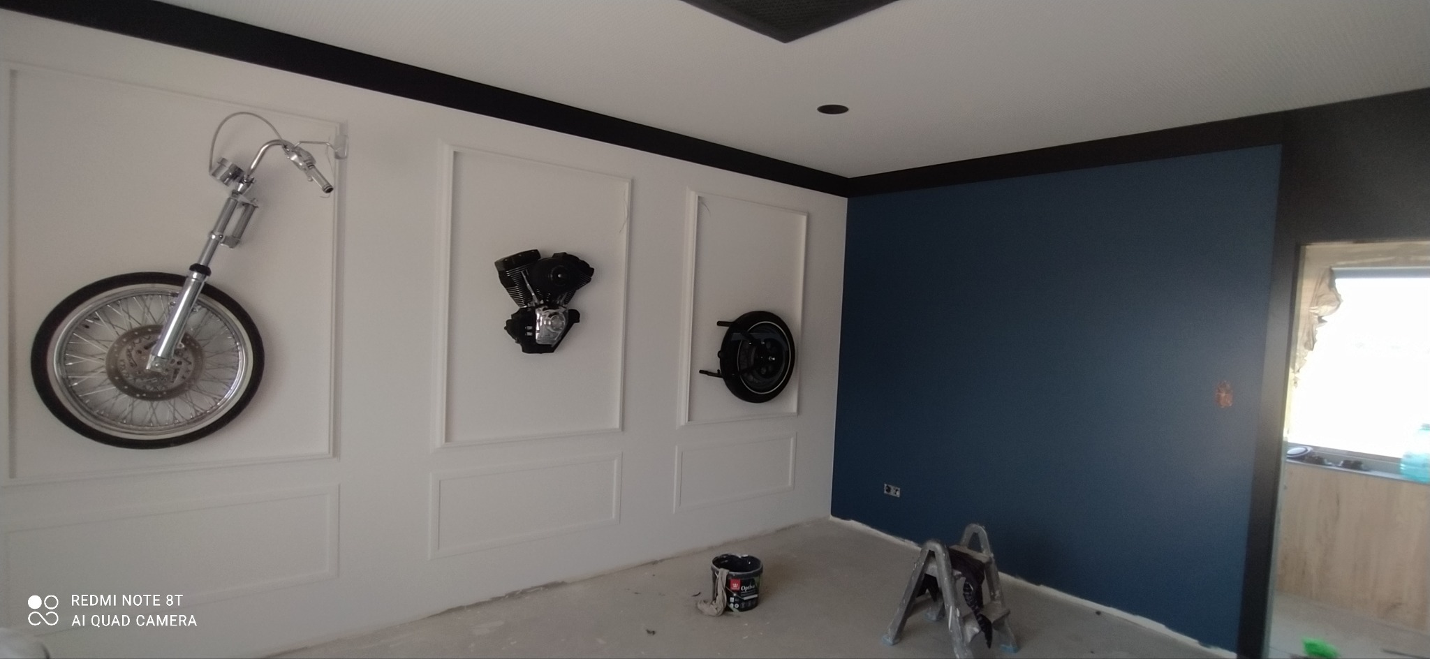 Pokój po malowaniu na granatowo z dekoracjami motoryzacyjnymi na ścianach. Widoczna drabina i puszka farby.