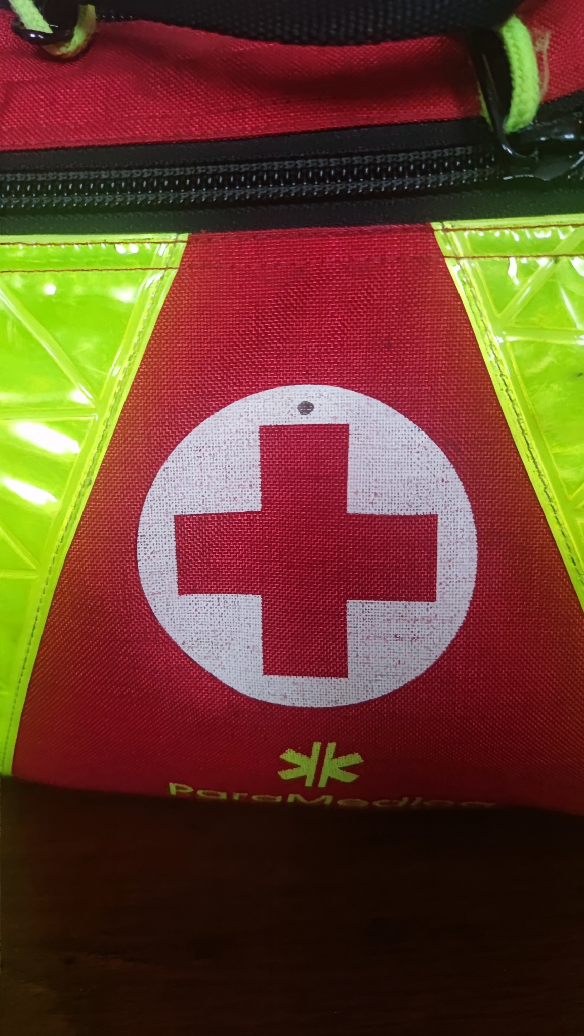 Czerwona torba medyczna z białym krzyżem na czerwonym tle i odblaskowymi elementami, widoczny zamek błyskawiczny i logo 'ParaMedic'.