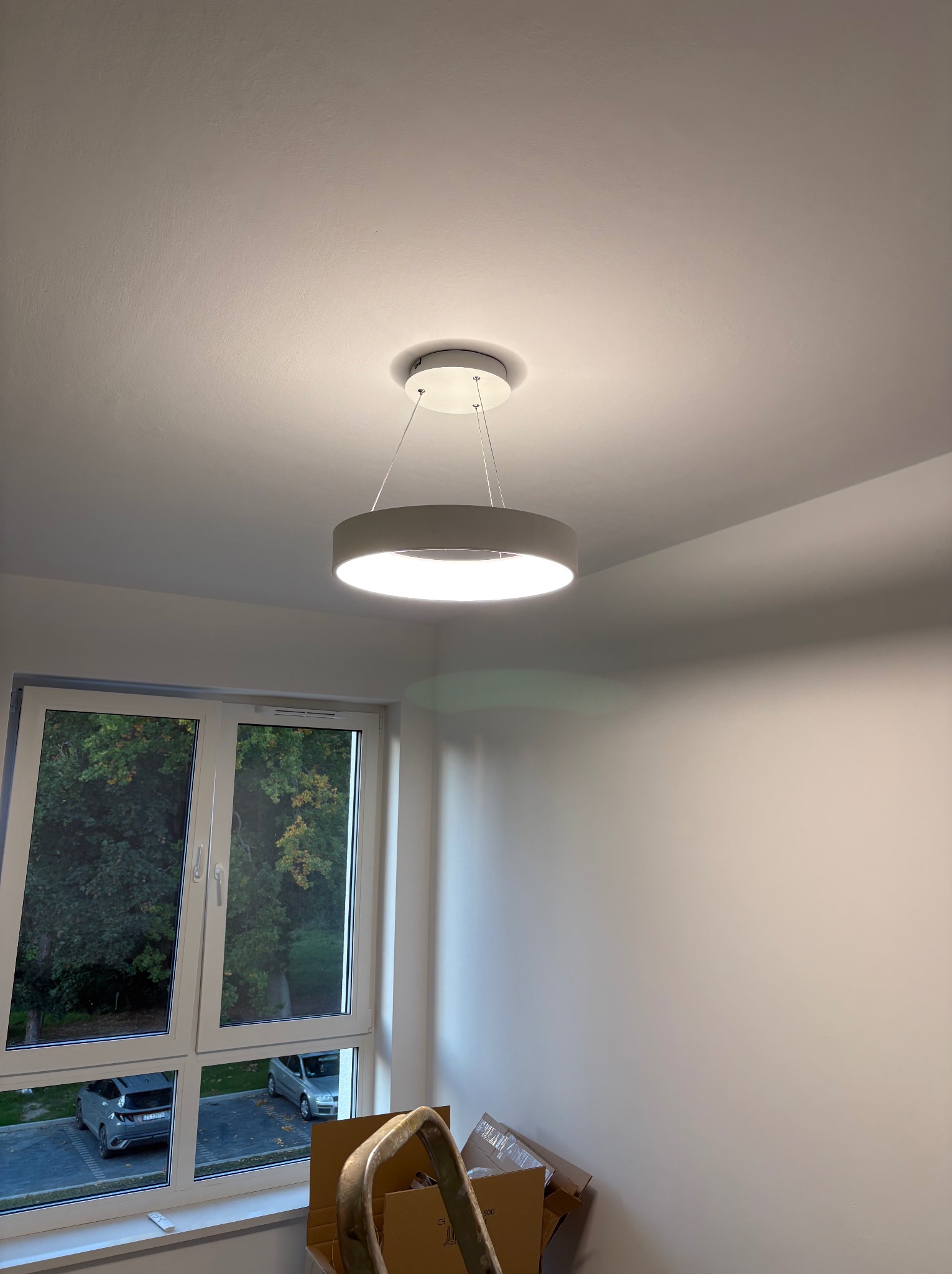 Nowoczesna, okrągła lampa sufitowa LED zawieszona w jasnym pokoju z oknem i częściowo widoczną drabiną, podkreślająca minimalistyczny design i oświetlenie.