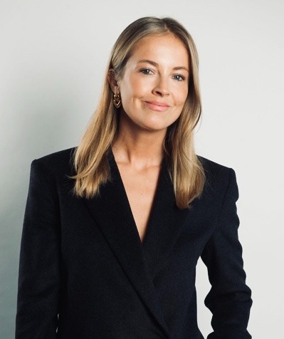 Profesjonalny portret kobiety w czarnym żakiecie, z delikatnym uśmiechem i złotymi kolczykami, na jasnym tle.