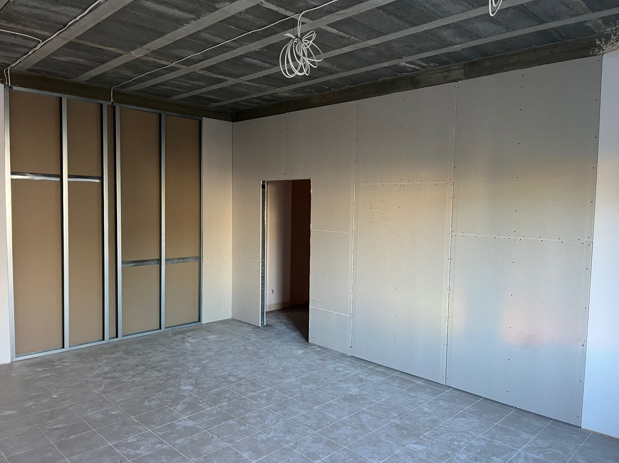 Wnętrze w trakcie montażu ścian działowych z płyt gipsowo-kartonowych, widoczne profile metalowe i instalacja elektryczna pod sufitem. Szare płytki na podłodze.