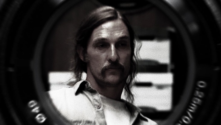 Czarno-biały portret mężczyzny z wąsami, widzianego przez obiektyw kamery, tworzący efekt wizualny kadrowania i głębi ostrości. Oświetlenie podkreśla rysy twarzy.