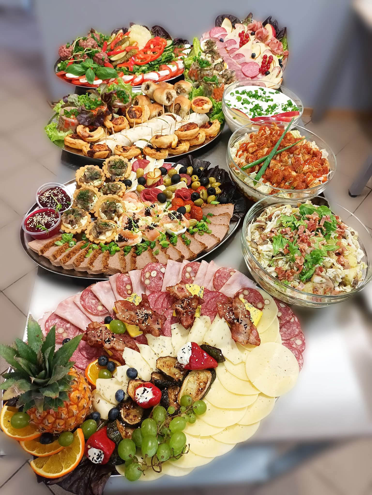 Bogato zastawiony stół z przekąskami: sałatki, koreczki, mięsa, sery i owoce. Różnorodność smaków i kolorów, idealne na przyjęcie.