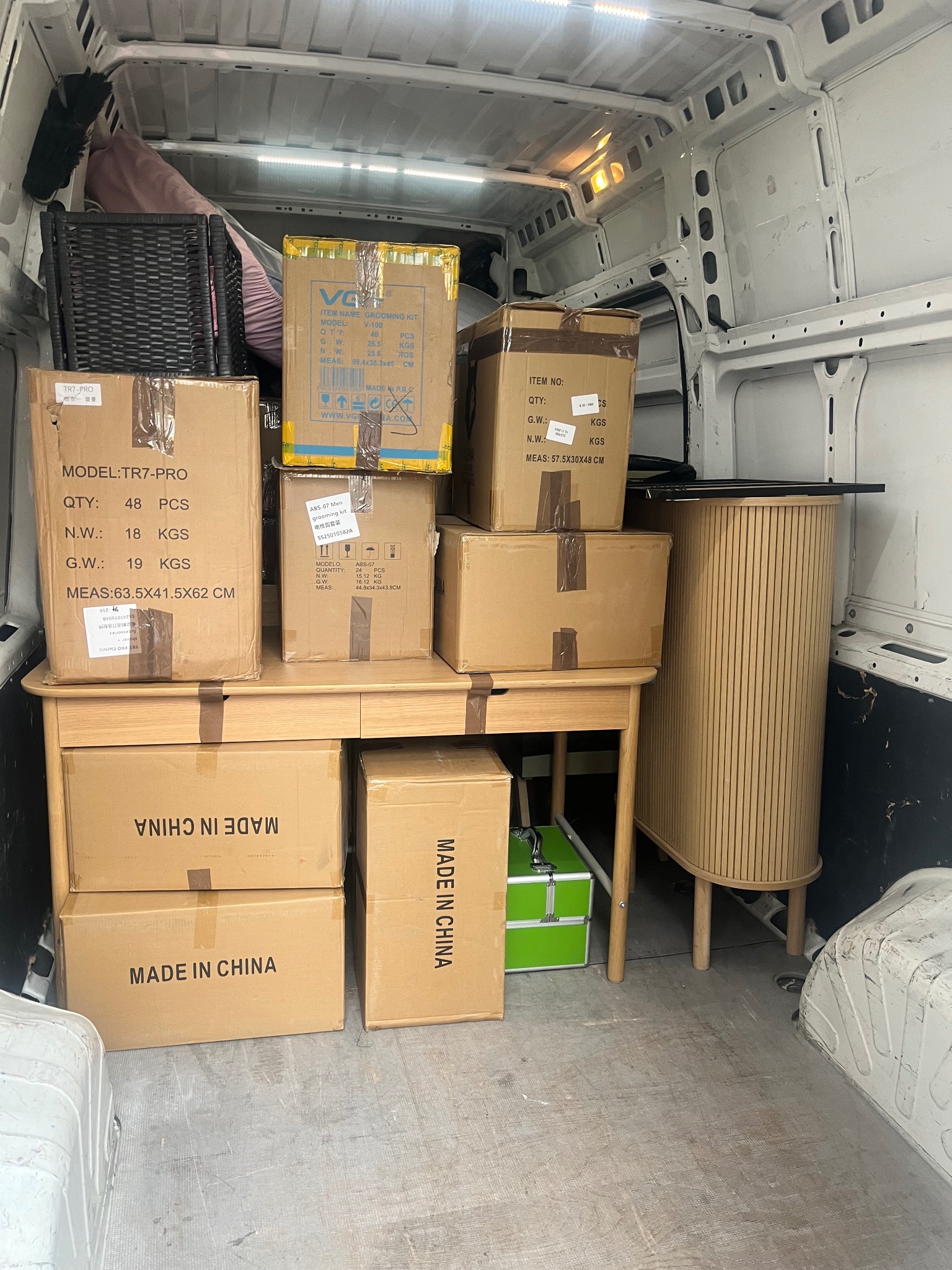 Wnętrze furgonetki wypełnionej kartonami z oznaczeniami 'MADE IN CHINA', skrzynką narzędziową i meblami gotowymi do transportu podczas przeprowadzki.