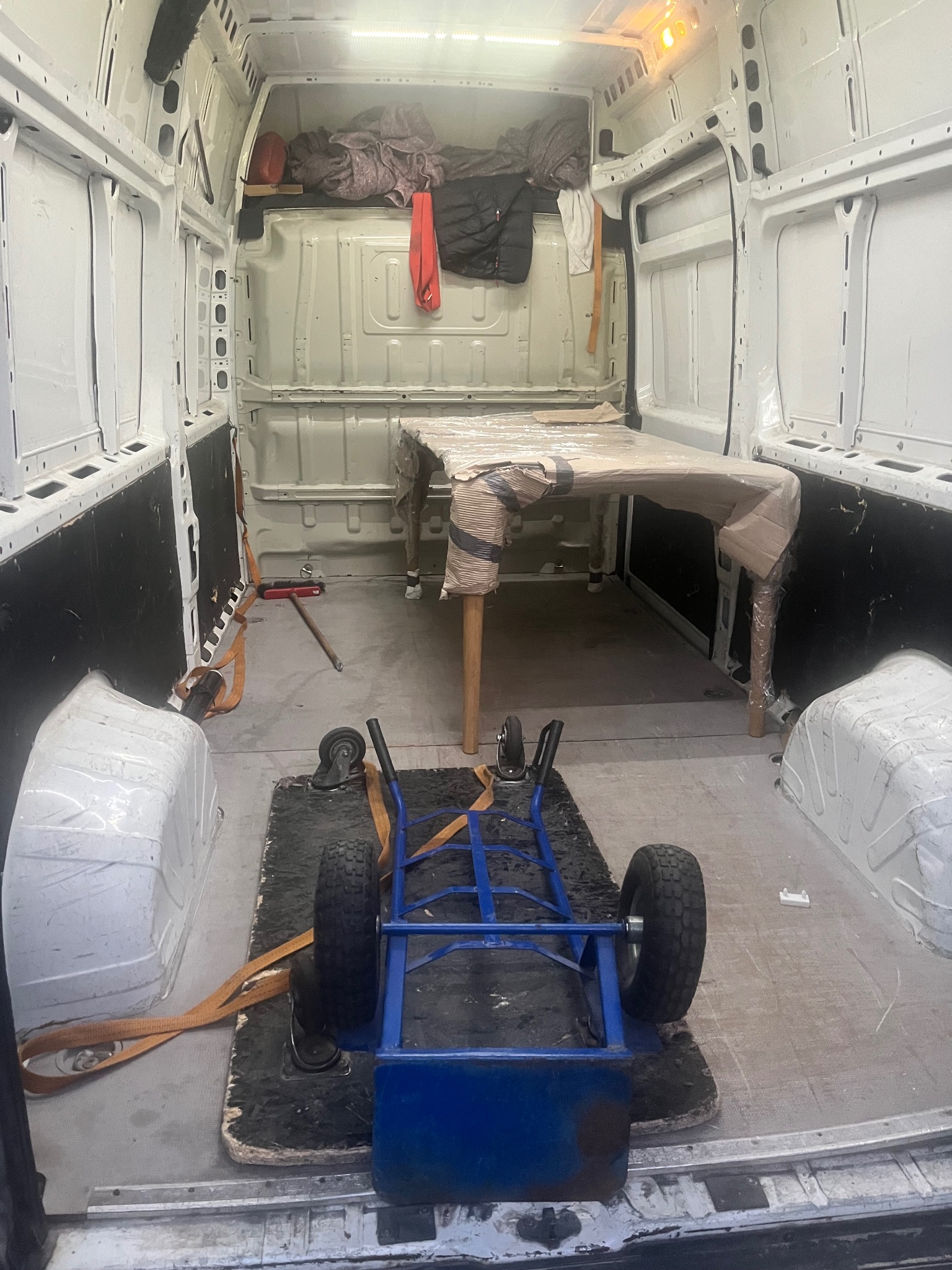 Wnętrze białej furgonetki z zabezpieczonym stołem i wózkiem transportowym. Widoczne pasy mocujące, gotowe do transportu mebli podczas przeprowadzki.