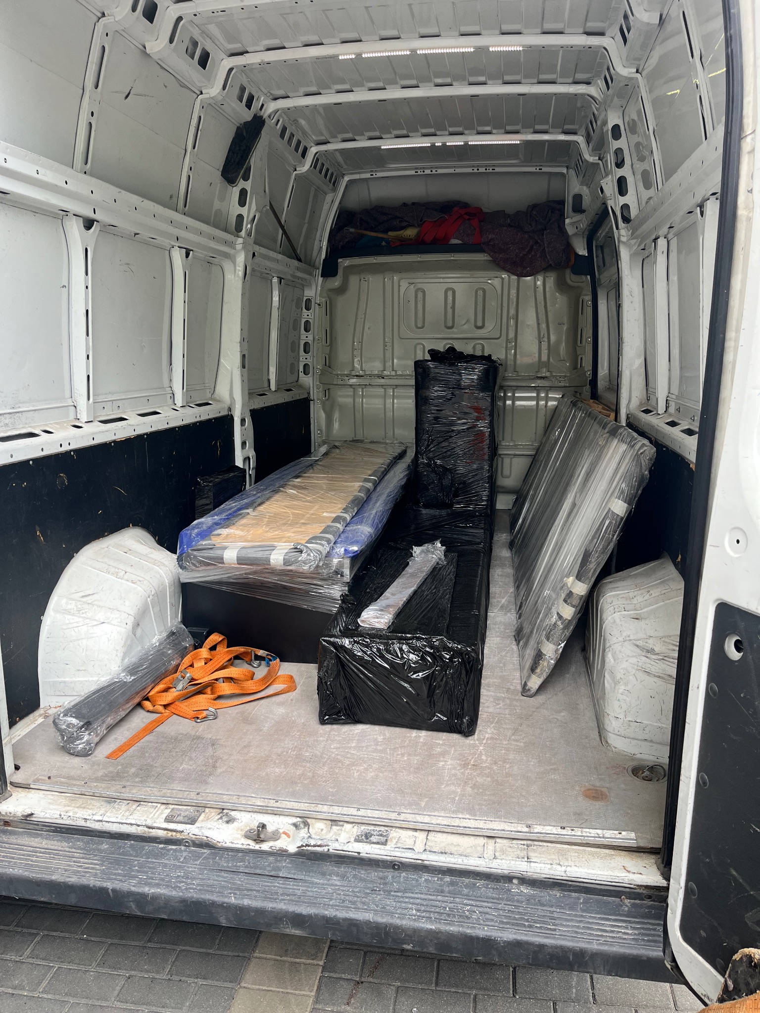 Wnętrze busa załadowane meblami zabezpieczonymi folią stretch i pasami transportowymi, gotowe do transportu. Widok z tyłu pojazdu.