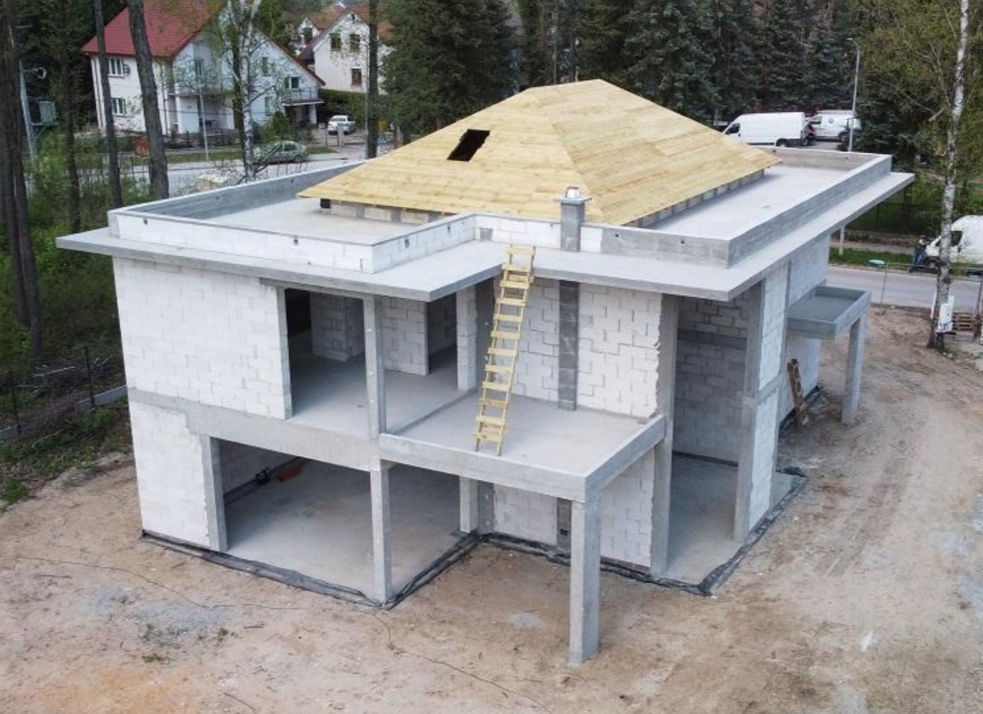 Dwukondygnacyjny budynek w stanie surowym otwartym z drewnianą konstrukcją dachu, drabina oparta o ścianę, widok z lotu ptaka.