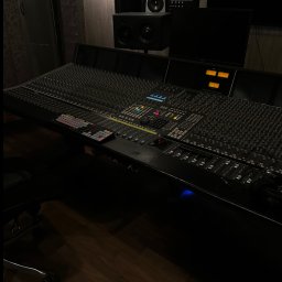 Hubert Popławski - Profesjonalna konsoleta mikserska w zaciemnionym studiu nagrań, z widocznymi głośnikami monitorowymi i parkietem. Sprzęt audio na pierwszym planie.