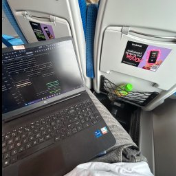 Hubert Popławski - Laptop z otwartym programem DAW w pociągu, butelka wody w siatce. Widoczny ekran z interfejsem edycji audio. Praca w podróży, mobilne studio nagrań?