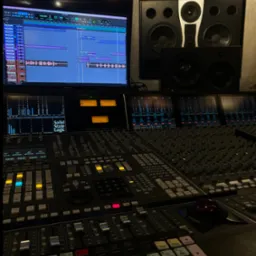 Profesjonalny stół mikserski Solid State Logic z monitorem DAW w studio nagrań. Widoczne głośniki studyjne. Oświetlenie ambientowe.