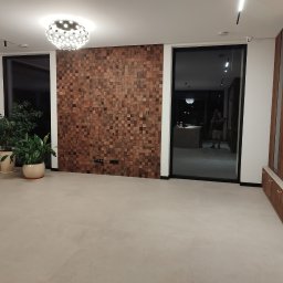 ArtDeco Renovations - Nowoczesne wnętrze z drewnianą ścianą z kwadratów, minimalistycznym oświetleniem i roślinami doniczkowymi. Widoczne duże okna i bio-kominek.