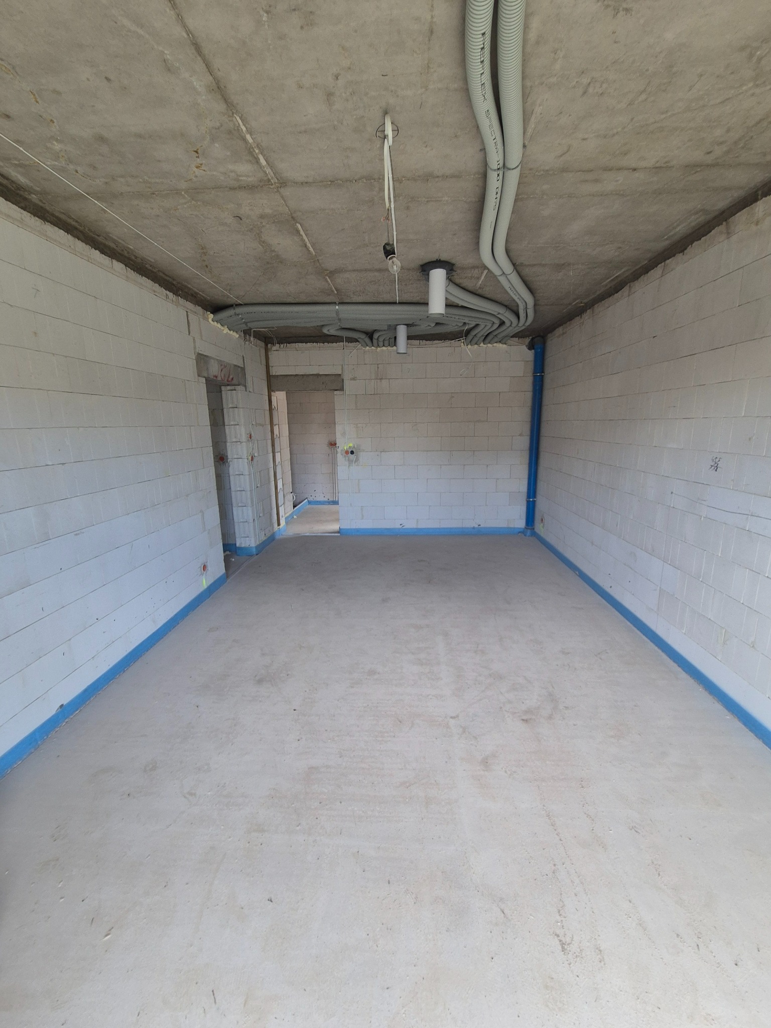 Surowy stan wnętrza: ściany z betonu komórkowego, instalacje w peszlach na suficie, przygotowane podłoże. Widok na surową przestrzeń w trakcie prac wykończeniowych.