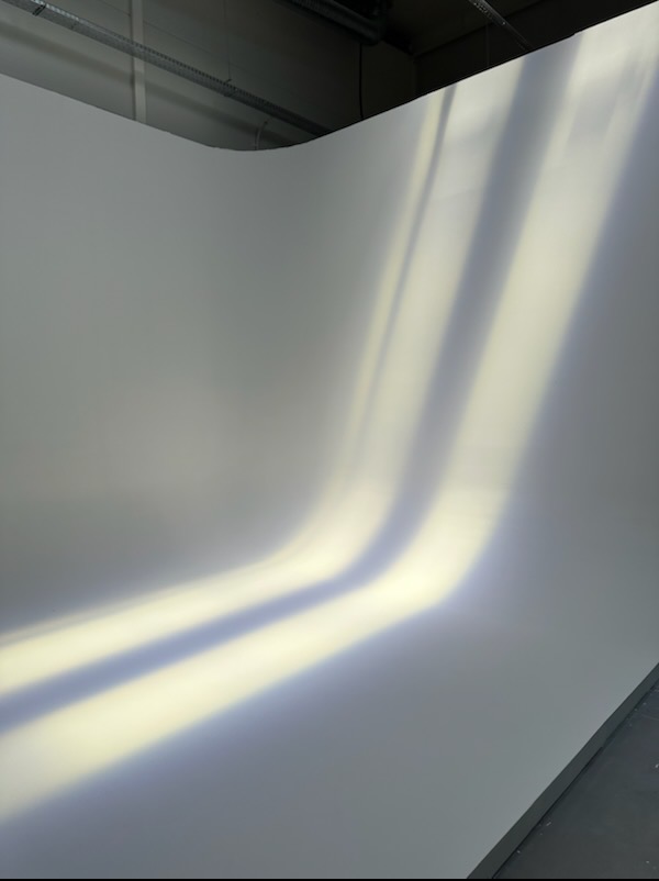 Biała ściana z efektem światła tworzącym łukowate cienie. Minimalistyczne ujęcie, podkreślające fakturę i grę światła na gładkiej powierzchni.