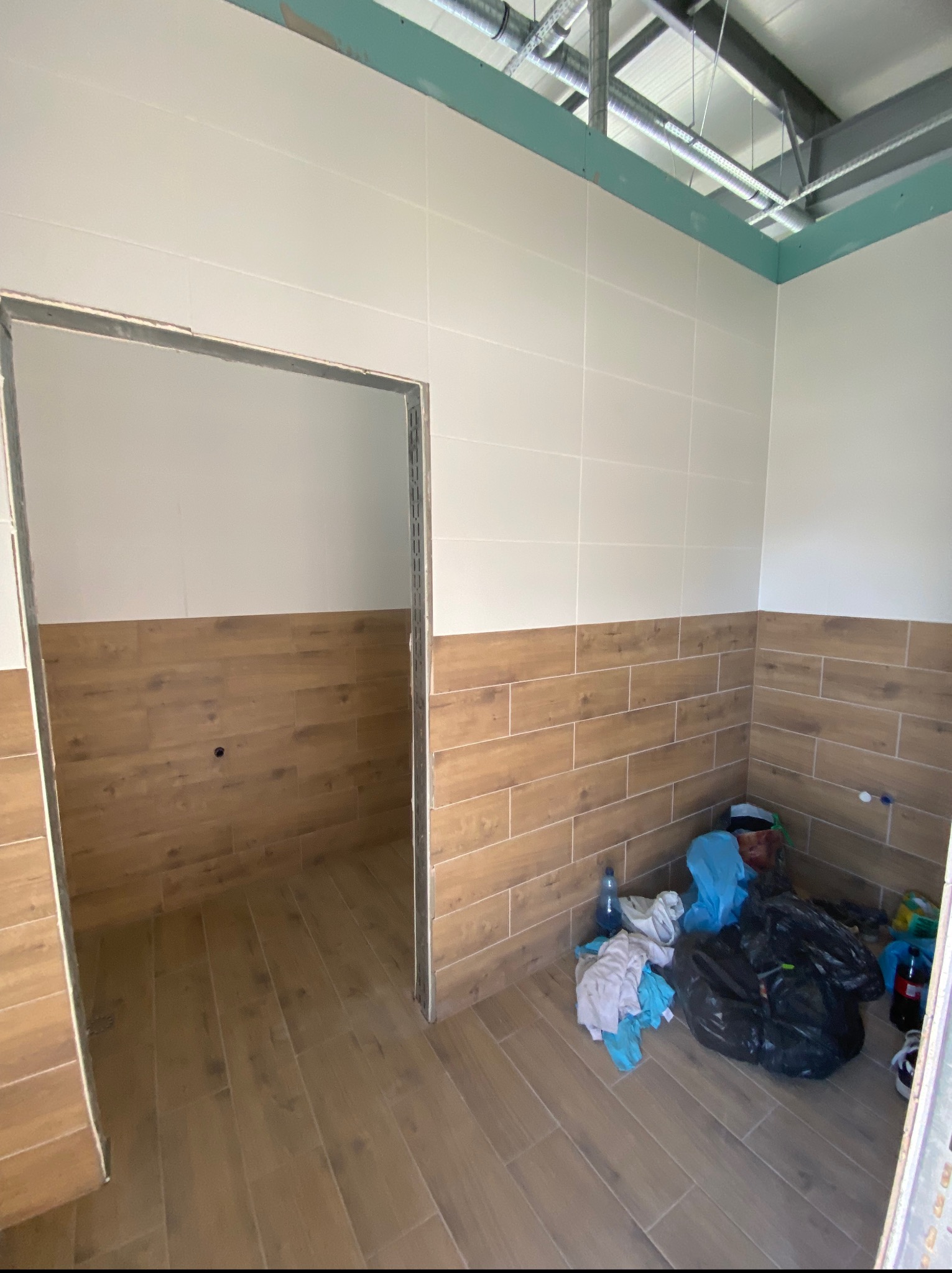 Wnętrze łazienki w trakcie prac wykończeniowych: położone płytki imitujące drewno na podłodze i ścianach do połowy wysokości, widoczne instalacje sufitowe i śmieci.