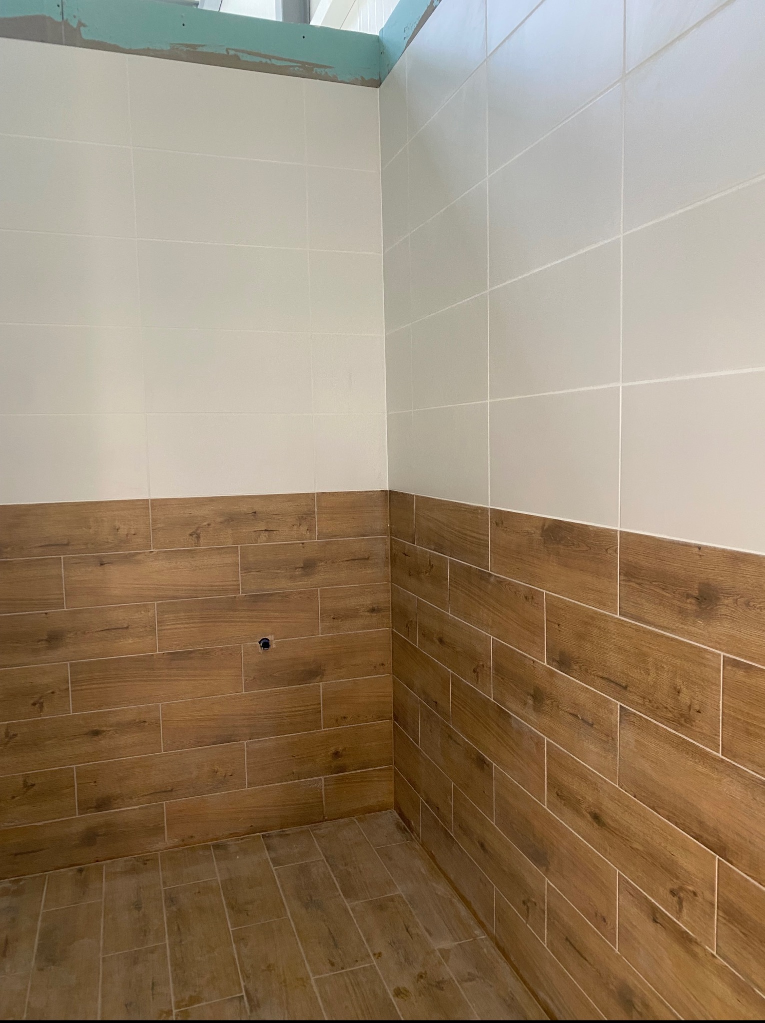 Wykończona łazienka z płytkami imitującymi drewno na dole i jasnymi płytkami na górze ścian. Widoczny fragment sufitu z płytą karton gips.