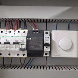 IT Technology - Wnętrze skrzynki elektrycznej z bezpiecznikami, zasilaczem i regulatorem temperatury. Widoczne przewody, elementy montażowe i oznaczenia. Estetyczne ułożenie przewodów.