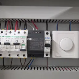 Wnętrze skrzynki elektrycznej z bezpiecznikami, zasilaczem i regulatorem temperatury. Widoczne przewody, elementy montażowe i oznaczenia. Estetyczne ułożenie przewodów.