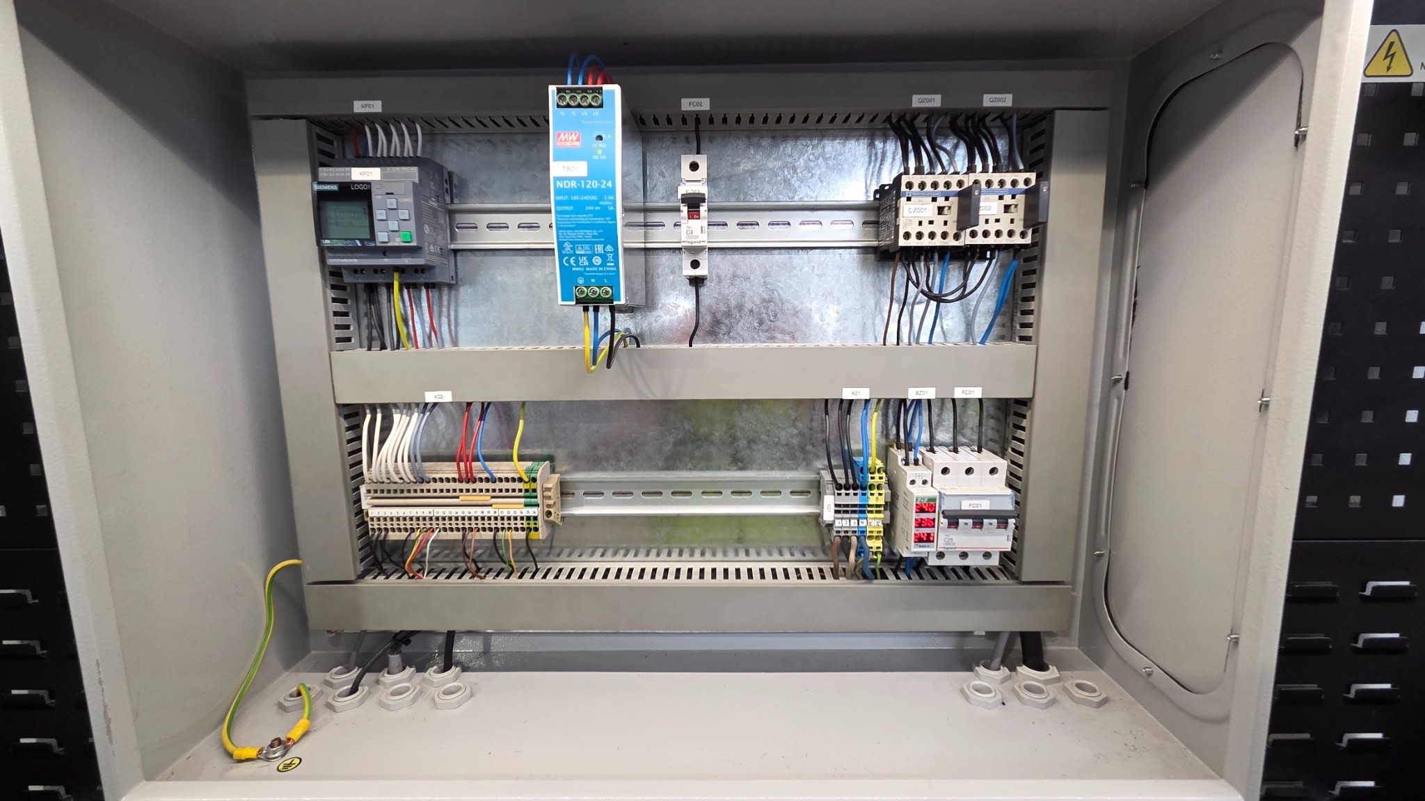 Rozdzielnica elektryczna w szarej obudowie z widocznymi elementami sterującymi, przewodami i zabezpieczeniami. Uwagę zwraca moduł Siemens LOGO! i zasilacz NDR-120-24.
