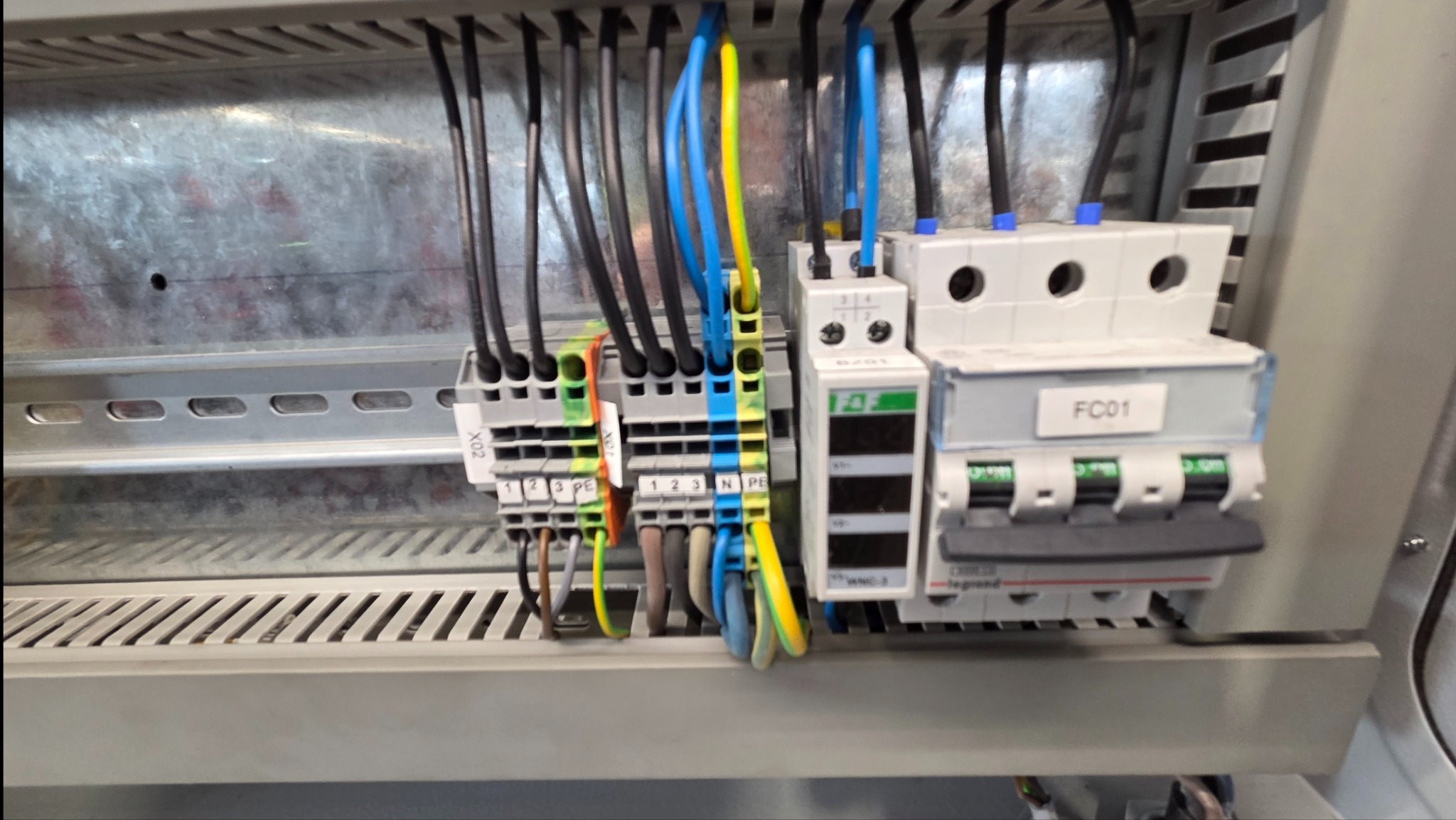 Szczegółowe ujęcie panelu elektrycznego z widocznymi przewodami, złączkami i wyłącznikami, ukazujące profesjonalny montaż instalacji wewnątrz szafy sterowniczej.