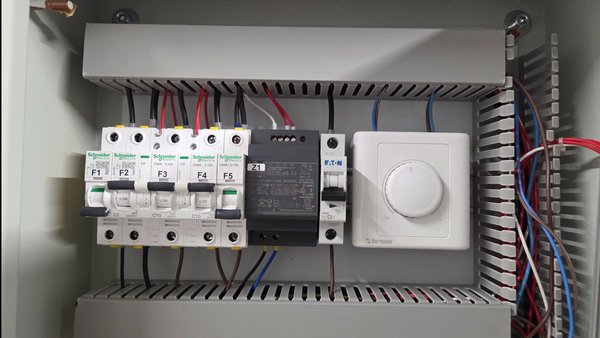 Wnętrze skrzynki elektrycznej z bezpiecznikami, zasilaczem i regulatorem temperatury. Widoczne przewody, elementy montażowe i oznaczenia. Estetyczne ułożenie przewodów.