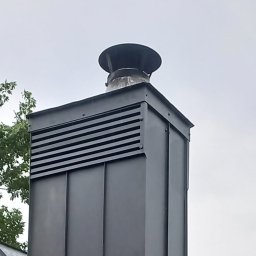 Marcin Głodowski - Metalowy komin wentylacyjny z daszkiem na dachu, widok z dołu, szare niebo w tle. Elementy blacharskie, nowoczesny design.