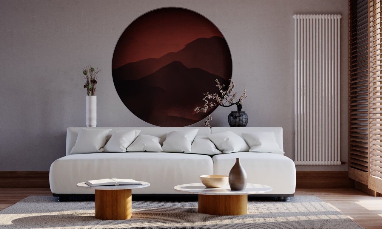 Minimalistyczny salon z białym narożnikiem, okrągłym obrazem górskim i drewnianymi akcentami. Stonowana kolorystyka i naturalne światło tworzą spokojną atmosferę.