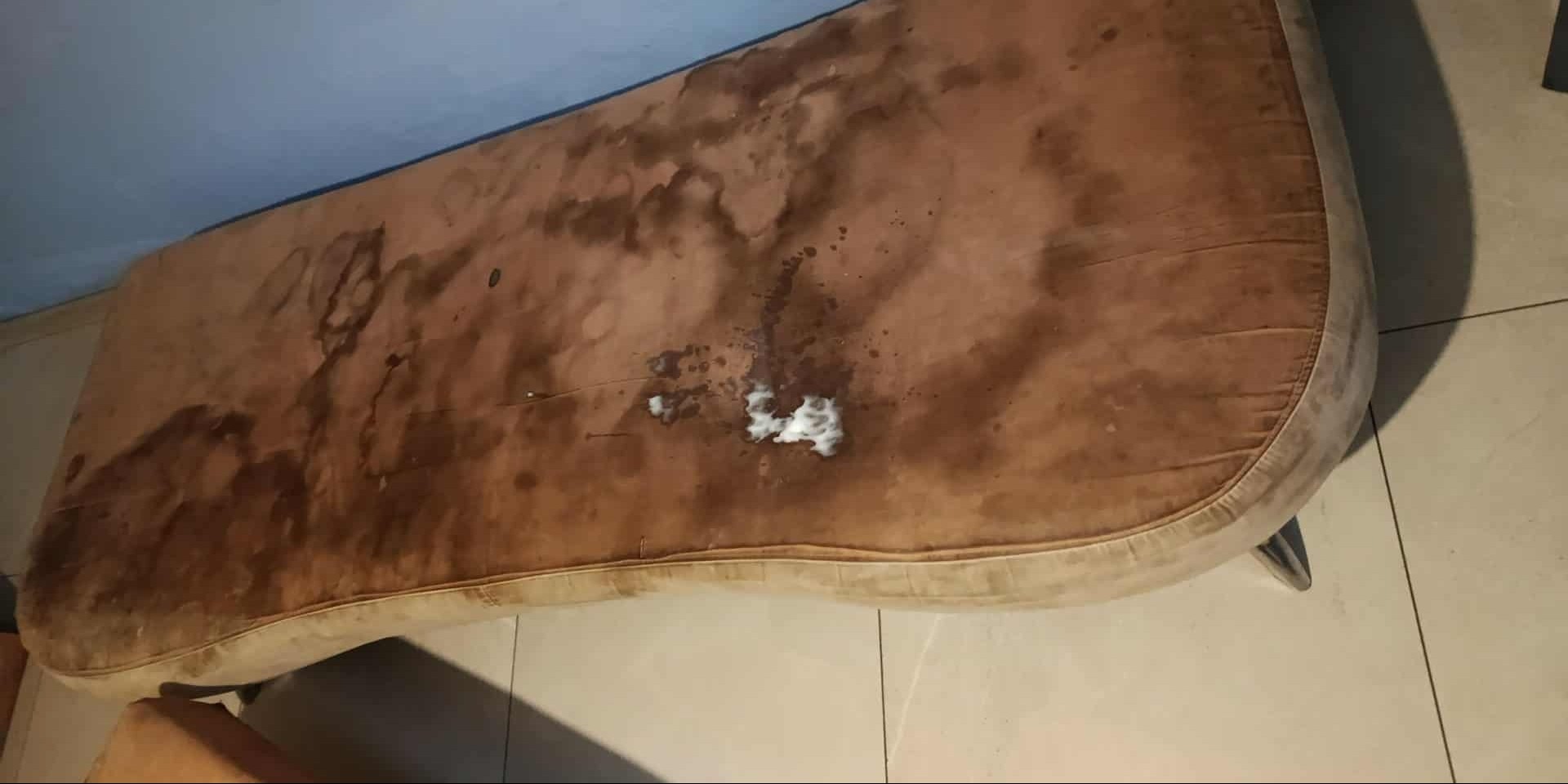 Brudny, mocno zaplamiony materac kanapy z widocznymi plamami i białym osadem, leżący na podłodze. Potrzebne odświeżenie tapicerki.