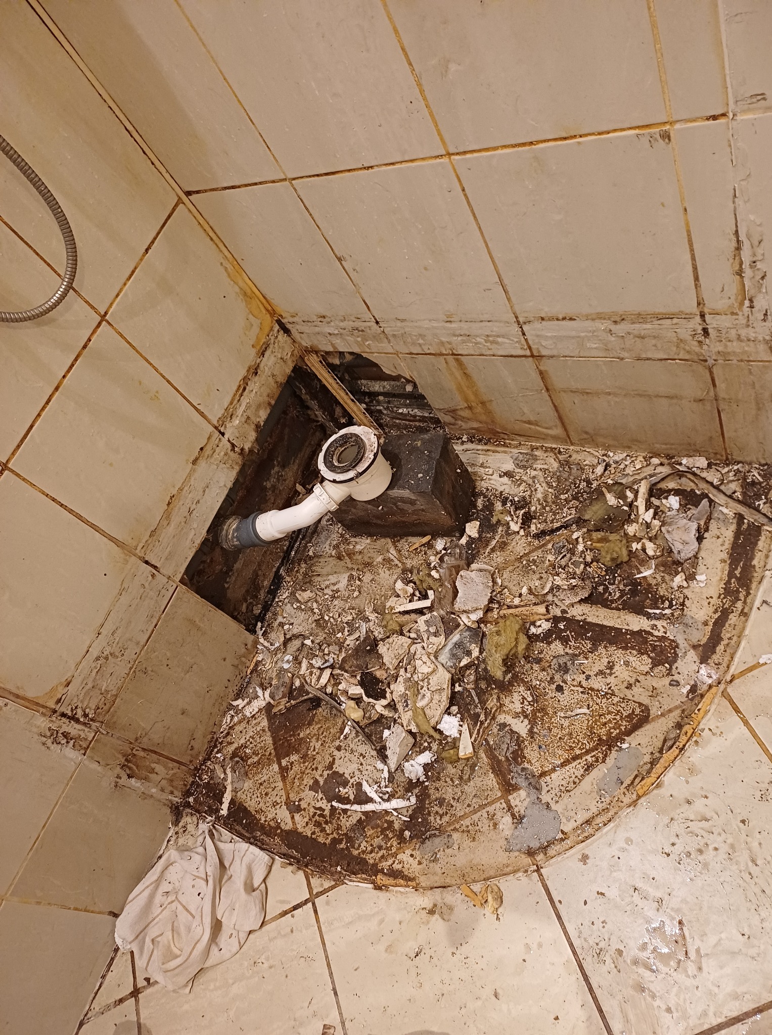 Odkryty odpływ prysznicowy w trakcie remontu łazienki, widoczne uszkodzone płytki i elementy instalacji. Ujęcie z góry na fragment podłogi.