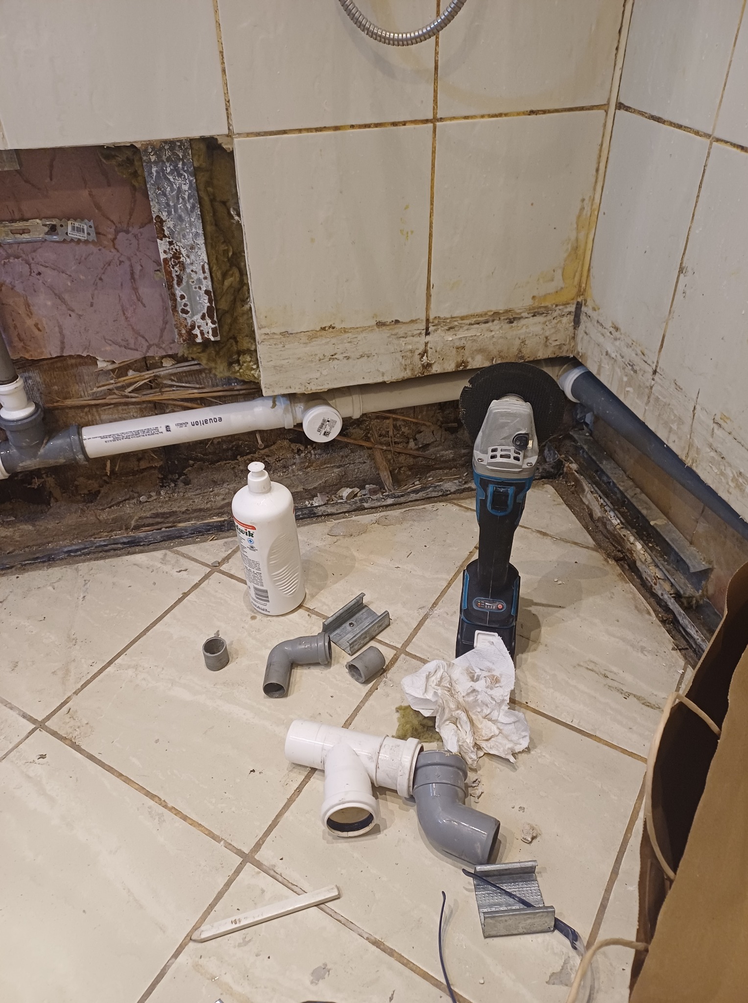Remont łazienki w trakcie: odkryte rury, narzędzia (szlifierka kątowa), płytki częściowo zdjęte, widoczna izolacja. Prace instalacyjne w starej łazience.