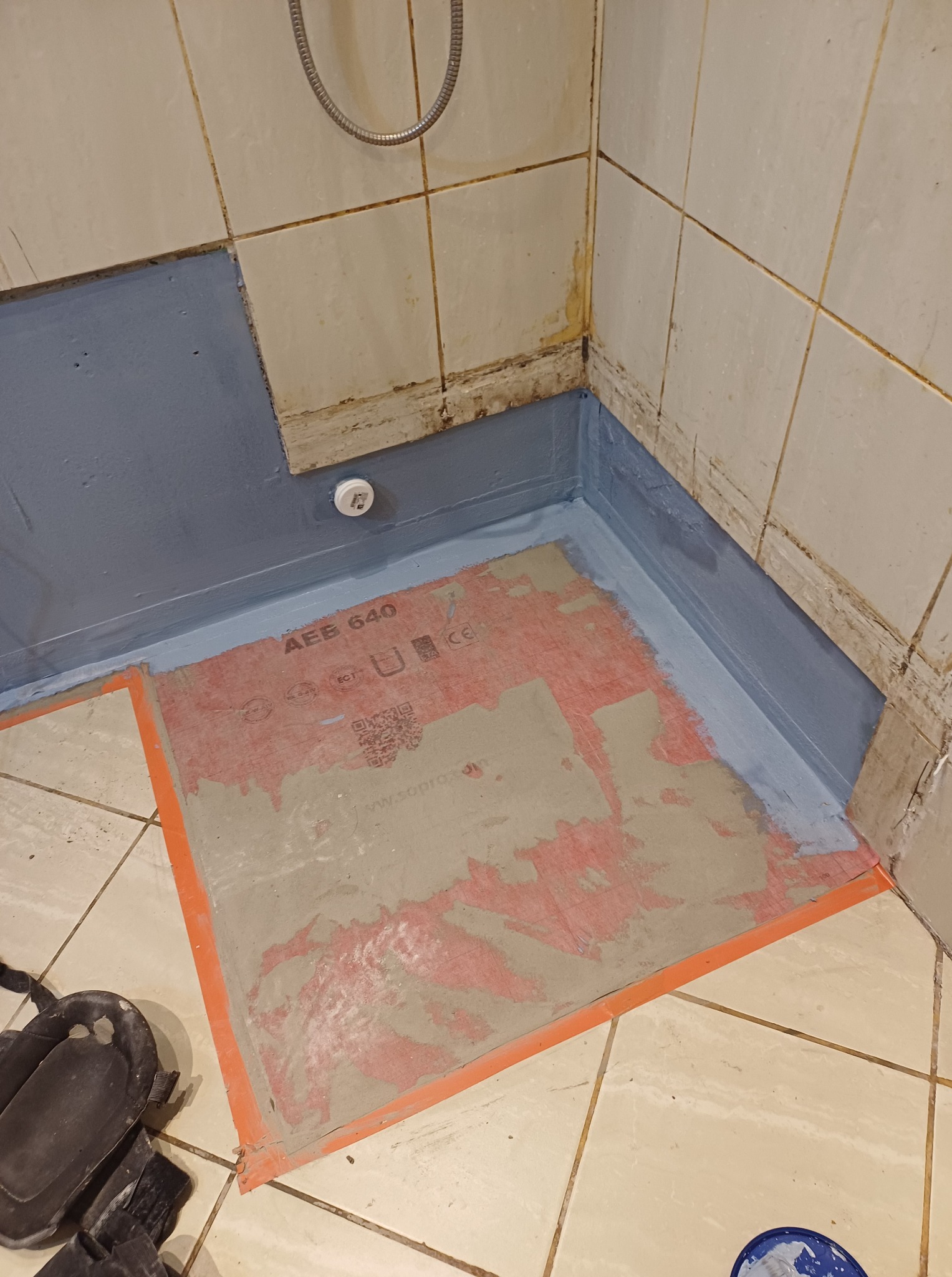 Przygotowanie brodzika do remontu: zabezpieczone ściany niebieską folią w płynie, na podłodze mata uszczelniająca z oznaczeniami, widoczne narzędzia pracy.