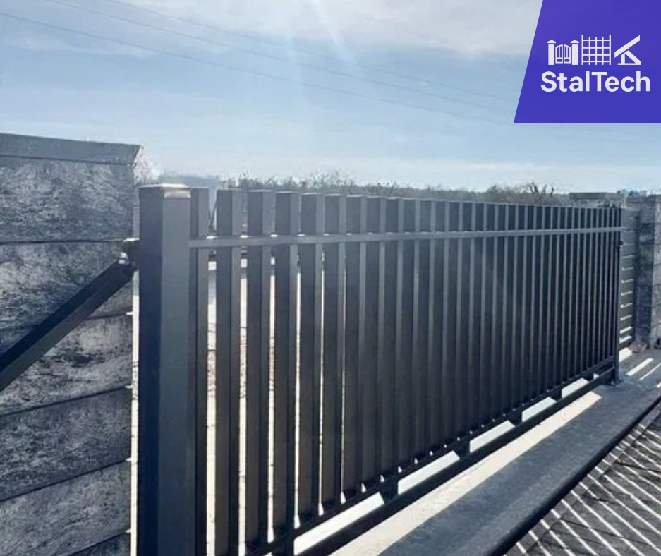 Nowoczesna brama wjazdowa z pionowymi profilami, zamontowana na betonowych słupkach. Widoczny mechanizm zawiasów. Brama w kolorze grafitowym.