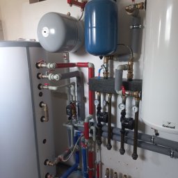 DE Systemy sp. z o.o. - Węzeł cieplny z zbiornikami wyrównawczymi i pompami obiegowymi w kotłowni w Warszawie. Instalacja wodna z zaworami i manometrami.