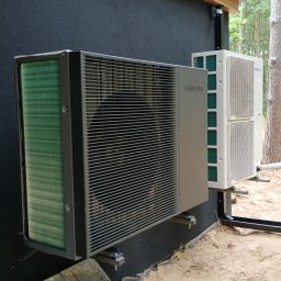 DE Systemy sp. z o.o. - Zewnętrzne jednostki klimatyzacji Samsung, zamontowane na ciemnej elewacji domu. Widoczne elementy montażowe i otoczenie budynku w trakcie prac instalacyjnych.