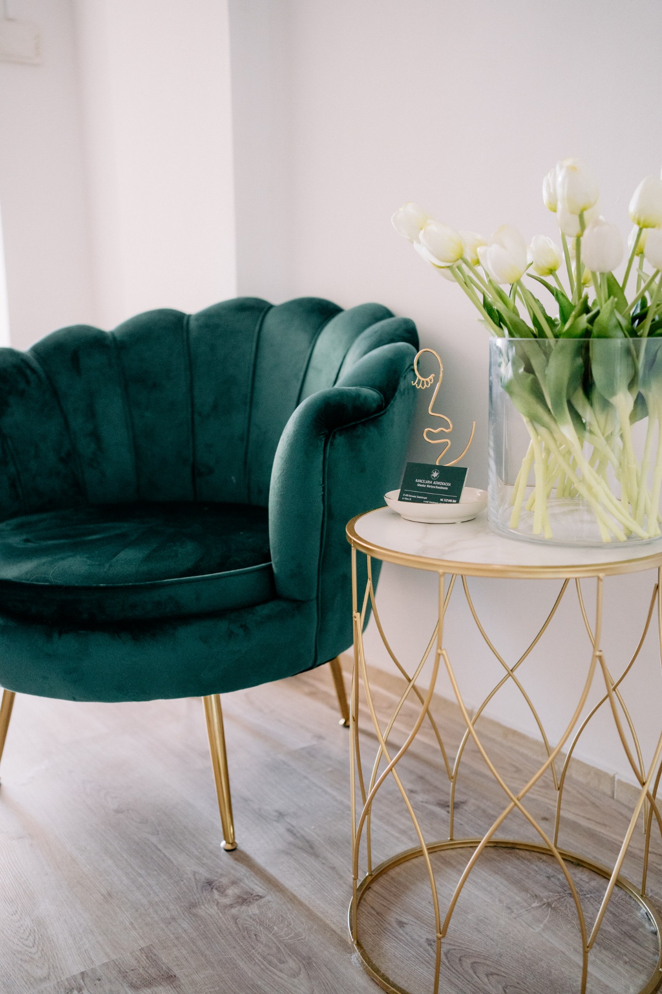 Elegancki gabinet: Szmaragdowy fotel, złoty stolik z tulipanami i wizytówka Kancelarii Adwokackiej, tworzące stylowe i profesjonalne wnętrze.