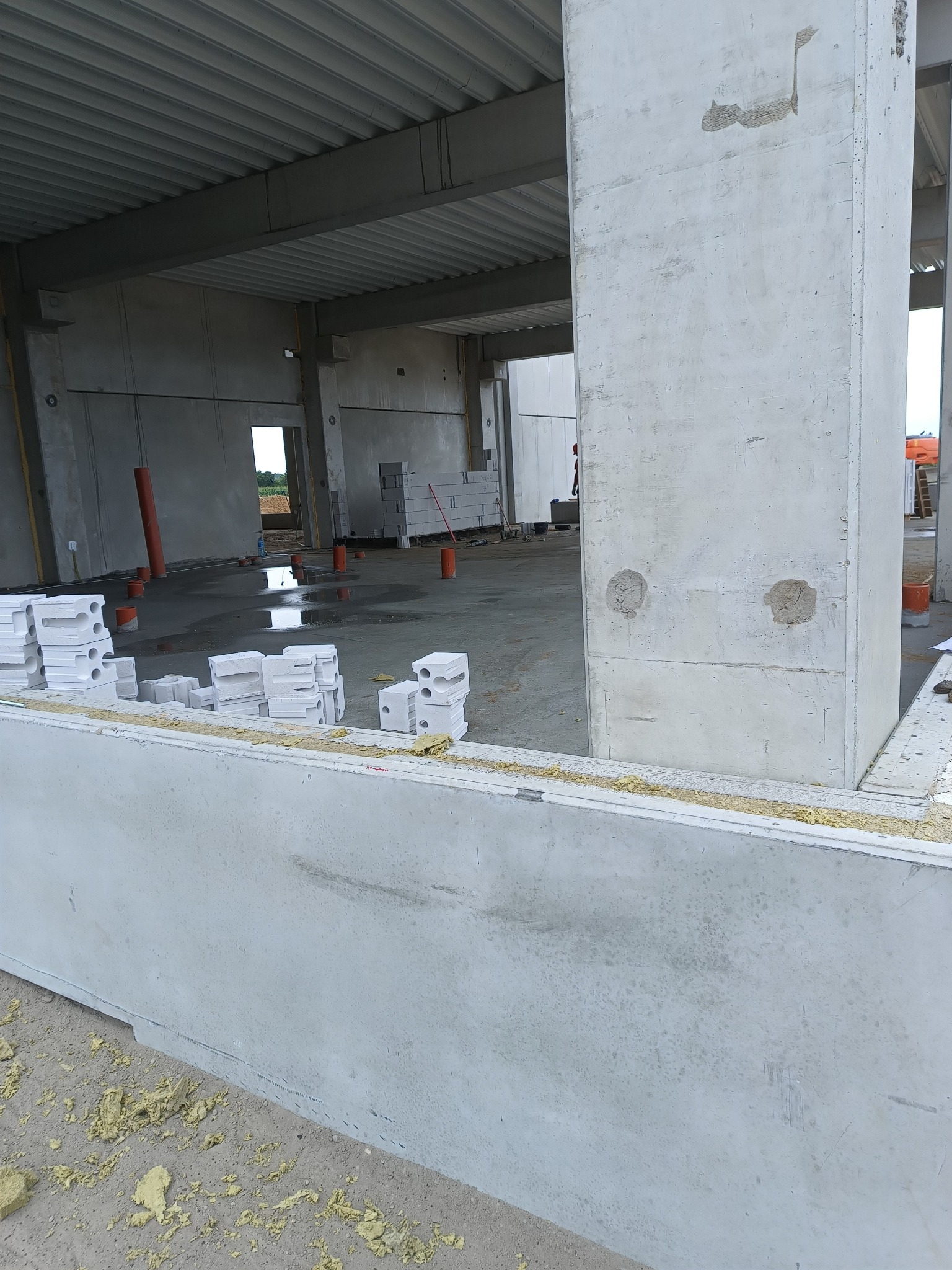 Wnętrze surowego budynku żelbetowego w trakcie budowy. Widoczne kolumny, ściany z betonu komórkowego, strop z blachy trapezowej i elementy izolacyjne.