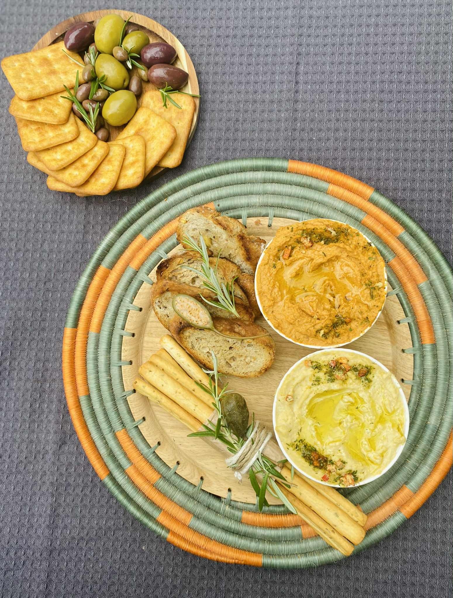 Dekoracyjna taca z przekąskami: hummus, pieczywo, grissini, oliwki i krakersy. Elegancki catering na imprezę w Łomiankach, gotowy do serwowania.