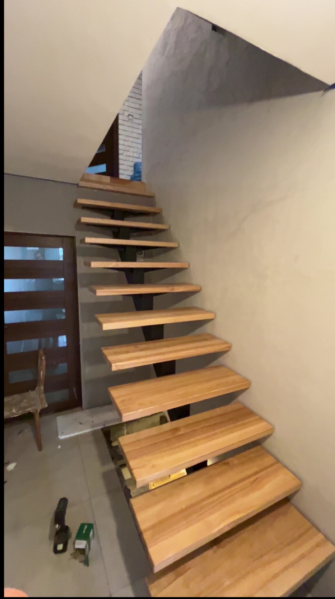 Nowoczesne schody drewniane wspornikowe z metalową konstrukcją, widok z dołu w trakcie montażu. Na podłodze narzędzia.