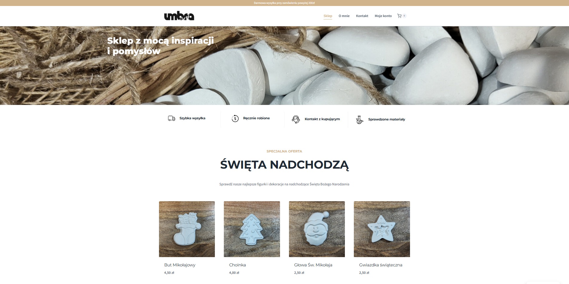 Strona internetowa sklepu Umbra z ofertą figurek świątecznych. W tle dekoracje z naturalnych materiałów. Widoczne ikony szybkiej wysyłki i ręcznej roboty.