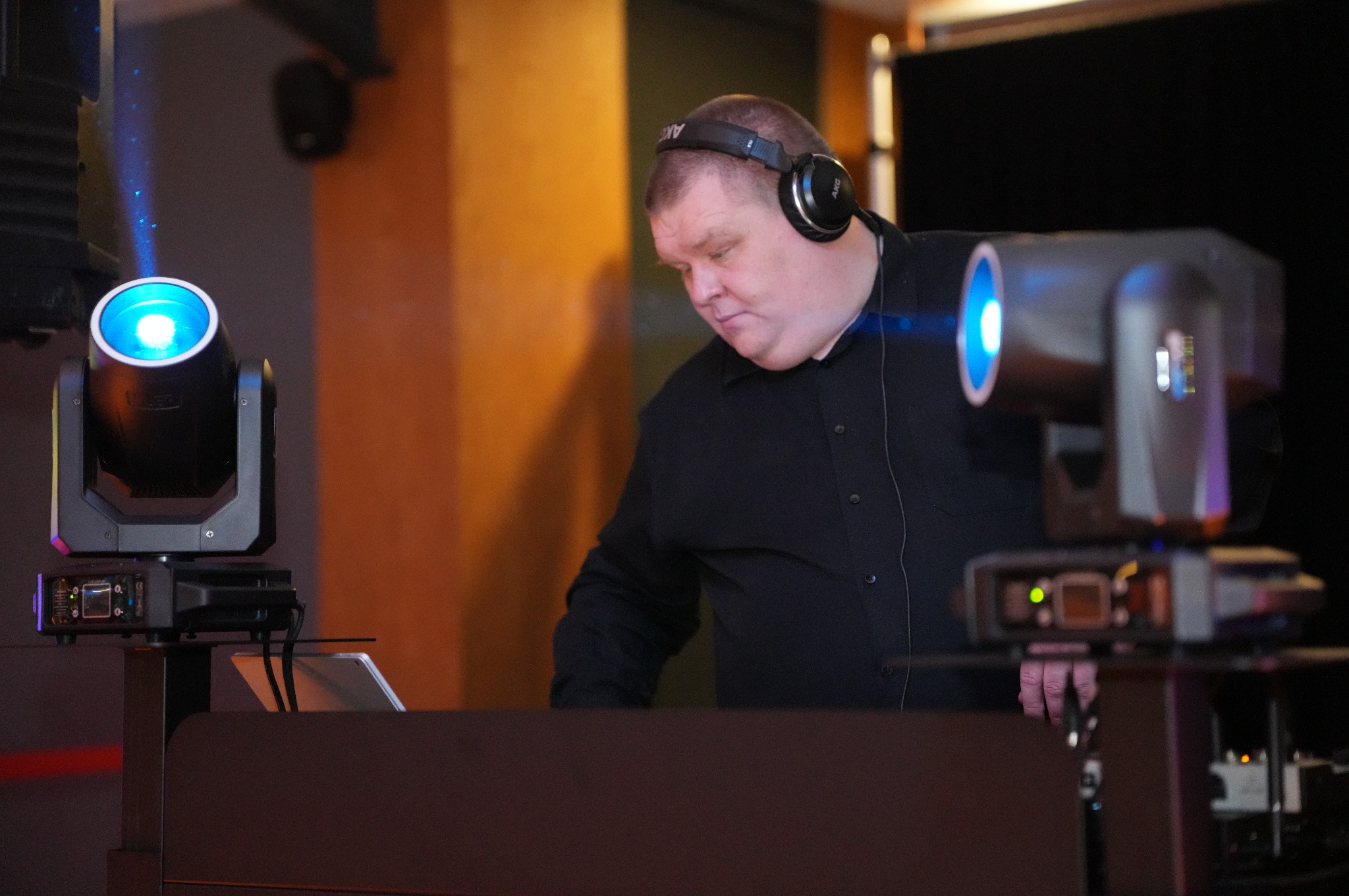Mężczyzna w słuchawkach obsługuje konsoletę oświetleniową z dwoma reflektorami scenicznymi emitującymi niebieskie światło podczas wydarzenia.