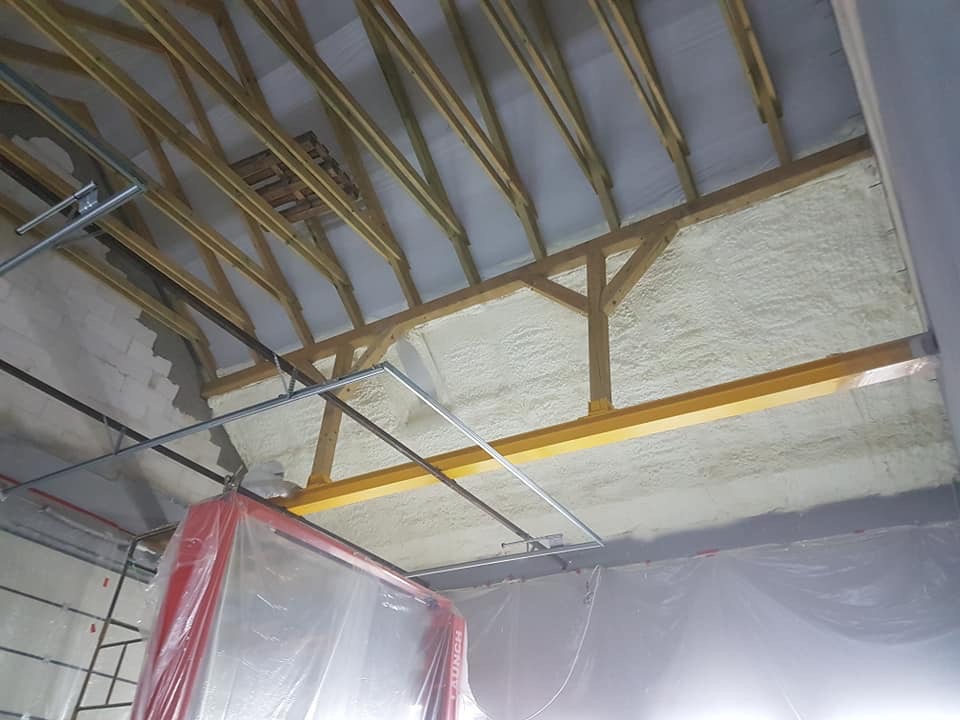 Poddasze z widoczną drewnianą konstrukcją dachu i ociepleniem pianką PUR, widoczne elementy rusztowania i zabezpieczenia folią malarską.